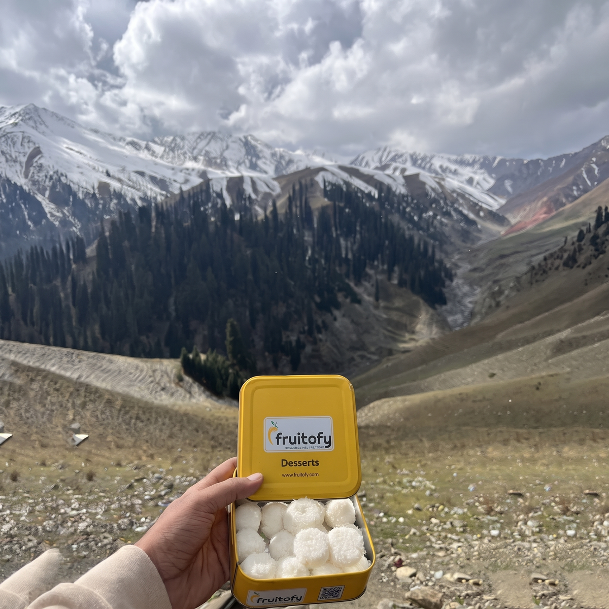 Open gold Fruitofy tin of Coconut Cloud held up in the mountains
